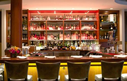 A stylish bar with a well-stocked shelf of various liquor bottles and a polished wooden counter with empty chairs.