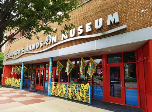 Exterior of a children's hands-on museum with colorful flags, bright red doors, and a welcoming entrance.
