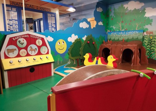 Colorful children's play area featuring a barnyard sounds panel, duck toys, and a vegetable garden backdrop.