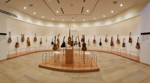 A circular display of various guitars on a wall in a well-lit gallery, showcasing musical instruments.