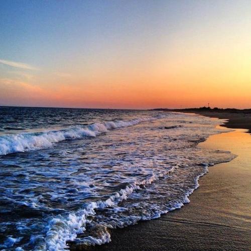 A serene beach at sunset, with gentle waves lapping at the shore under a colorful sky.