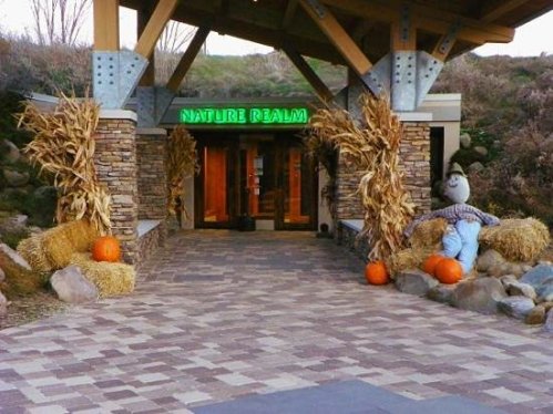 Entrance to Nature Realm, featuring stone pillars, corn stalks, pumpkins, and a scarecrow on hay bales.