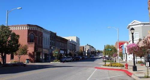 A sunny street view of a small town with shops, trees, and clear blue skies.