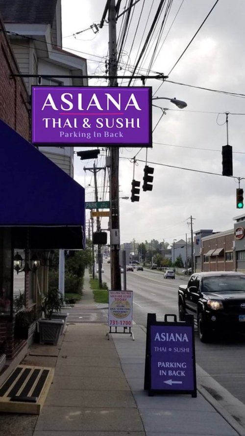 Sign for Asiana Thai & Sushi with a parking notice, located on a street with traffic lights and cloudy skies.