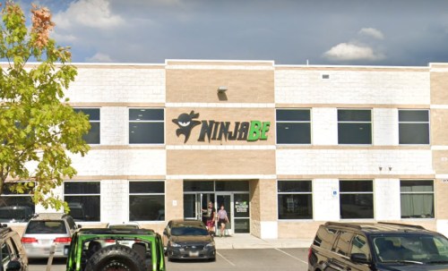 Exterior of a building with a large "NinjaBE" sign, featuring a tree and parked cars in front.