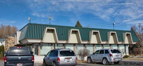 A modern building with a green roof and large windows, surrounded by parked cars under a clear blue sky.