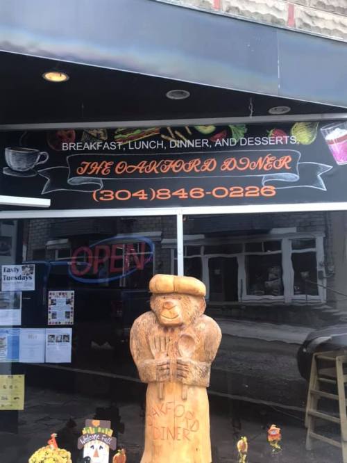 Sign for "The Oakford Doner" featuring breakfast, lunch, dinner, and desserts, with a wooden bear statue outside.