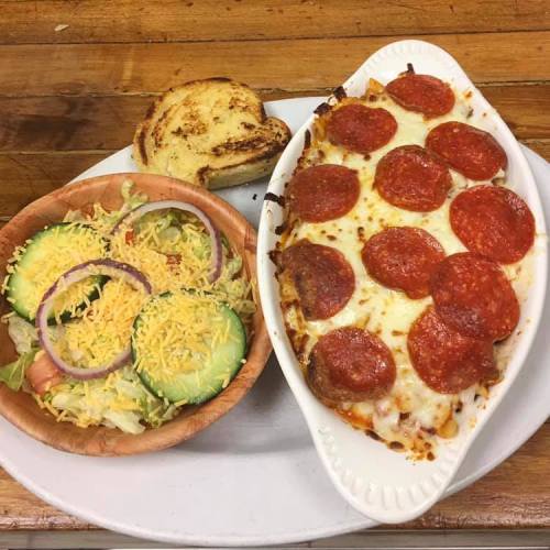 A plate featuring cheesy pepperoni pasta bake, a side salad with cucumbers and cheese, and a toasted bread slice.