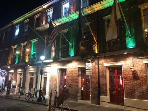 A historic brick building at night, illuminated with green and yellow lights, featuring flags and bicycles outside.