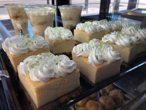 A display of creamy cheesecake squares topped with whipped cream and lime zest, alongside dessert cups.