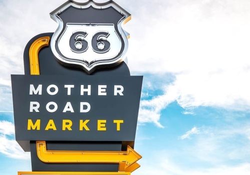 Sign for Mother Road Market with Route 66 emblem against a blue sky.