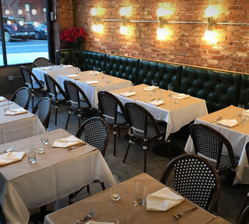 Cozy restaurant interior with brick walls, green banquettes, and neatly set tables with white linens and glassware.