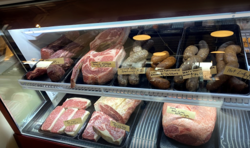 A display case filled with various cuts of meat, including steaks and sausages, labeled with prices.