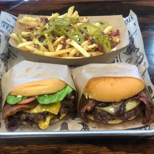 A tray with two wrapped burgers and a side of loaded fries topped with jalapeños and bacon.