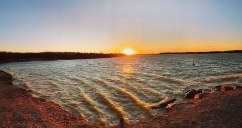 A serene sunset over a lake, with gentle waves and a clear sky, casting warm colors on the water's surface.
