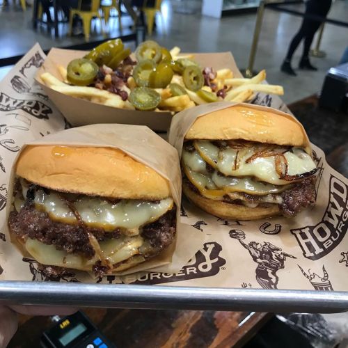Two cheeseburgers with melted cheese and grilled onions, served with a side of fries topped with jalapeños.