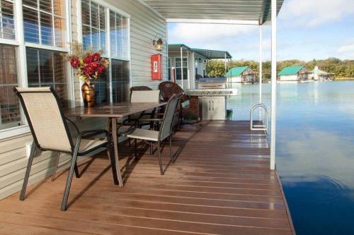 A cozy outdoor dining area on a wooden deck by the water, featuring a table, chairs, and a grill.
