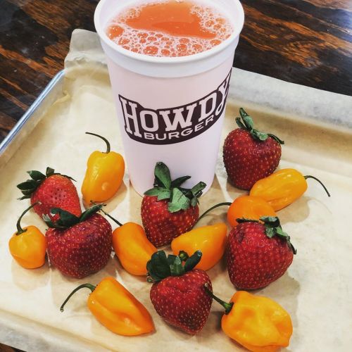 A cup of orange drink next to fresh strawberries and yellow peppers on a tray.