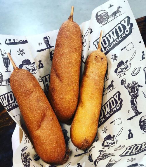 Three golden-brown corn dogs on a patterned paper, served at Howdy Burger.