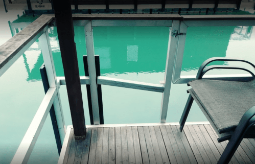 A wooden deck with a metal railing and a chair overlooking calm, turquoise water.