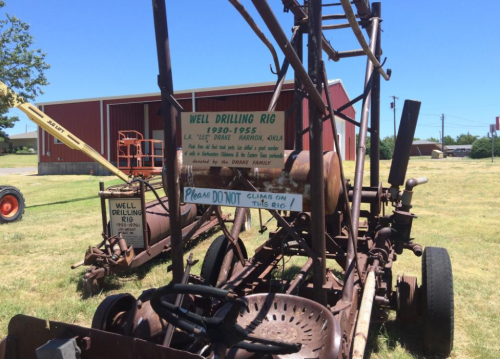 A vintage well drilling rig with a sign reading "Please DO NOT climb on this rig," set in a grassy area.