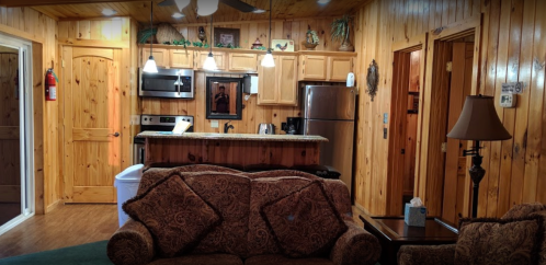 Cozy wooden cabin interior featuring a living area, kitchen with appliances, and warm lighting.