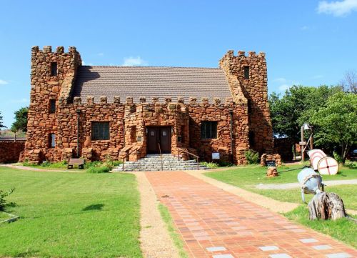 A stone building with a castle-like design, surrounded by green grass and a pathway leading to the entrance.