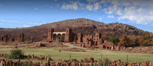 Ruins of stone buildings on a grassy landscape, with a hill and blue sky in the background.