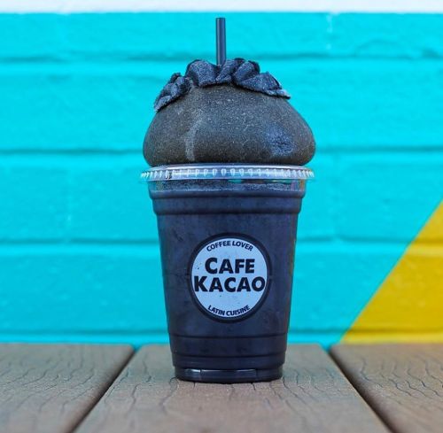 A dark, charcoal-flavored drink topped with a unique black foam, served in a clear cup with a straw.