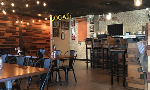Cozy restaurant interior with wooden accents, bar seating, and warm lighting, featuring a "LOCAL" sign.