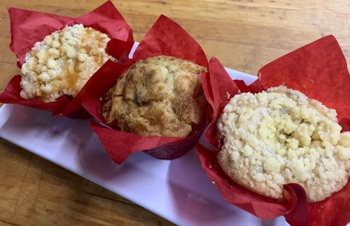 Three muffins with colorful red wrappers, displayed on a white plate, featuring crumbly tops and varying textures.