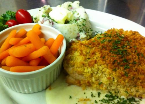 A plate featuring baked chicken with a crispy topping, mashed potatoes, glazed carrots, and cherry tomatoes.