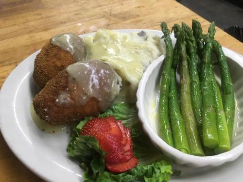 A plate with two breaded croquettes, creamy mashed potatoes, asparagus, and a strawberry on a bed of lettuce.