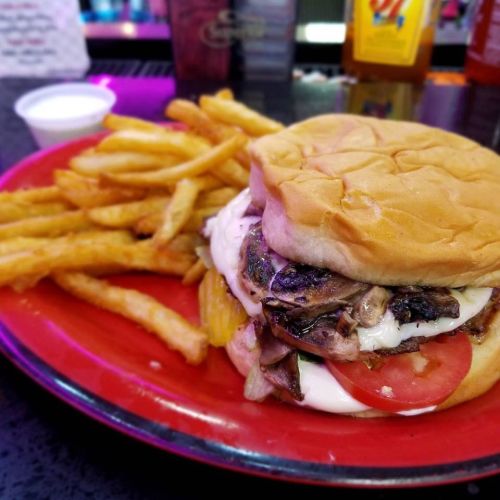 A juicy burger with grilled mushrooms, lettuce, tomato, and mayo, served with a side of crispy French fries.