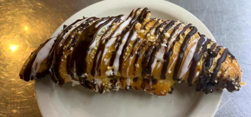 A pastry drizzled with chocolate and icing, sitting on a white plate against a metallic background.