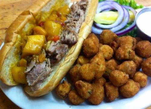 A pulled pork sandwich with mango salsa, served with fried okra and fresh vegetables on the side.