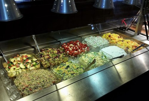 A variety of colorful salads and fruits displayed in clear containers on a buffet table.