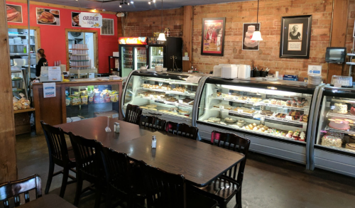 A cozy café interior featuring a display case of desserts, a wooden table, and a counter with a staff member.