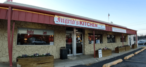 Exterior of Ingrid's Kitchen restaurant, featuring a red roof, stone walls, and flower planters, with an "Open" sign.