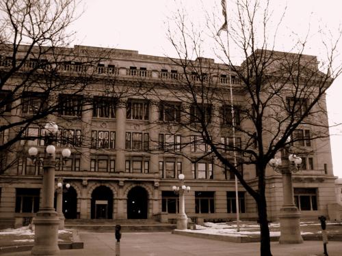 Historic building with ornate architecture, large windows, and bare trees in front, captured in sepia tones.