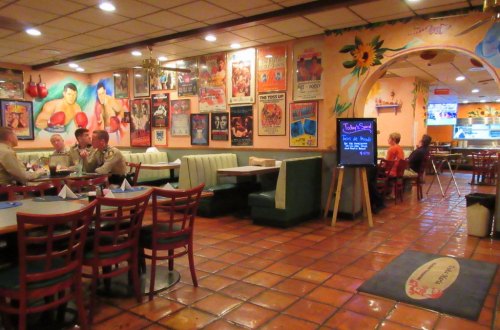 A colorful restaurant interior with booths, vibrant wall art, and patrons dining at tables.