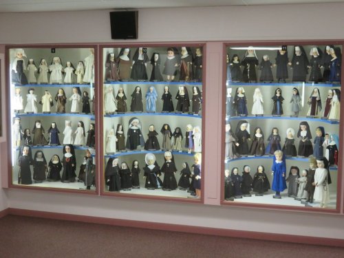 A display case filled with various dolls dressed in religious attire, showcasing a range of styles and expressions.