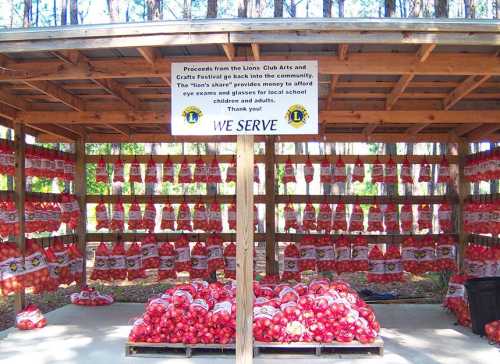 A wooden stand displaying bags of apples, with a sign about community support from the Lions Club Arts and Crafts Festival.