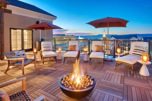 A cozy rooftop terrace with lounge chairs, umbrellas, and a fire pit, overlooking a scenic sunset.