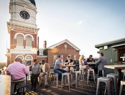 People enjoying drinks on a rooftop bar with a clock tower in the background during sunset.
