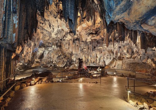 A vast cave interior with dramatic stalactites and stalagmites, illuminated by soft lights on the stone floor.