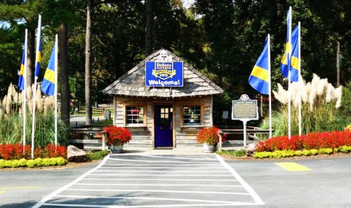 A wooden welcome center with flags and colorful flowers, surrounded by trees in a park setting.