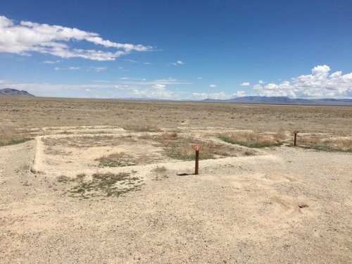 A barren landscape with a rectangular foundation outline and sparse vegetation under a clear blue sky.