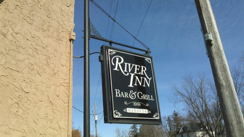 Sign for "River Inn Bar & Grill" in Hanover, featuring a black background with white lettering against a clear blue sky.