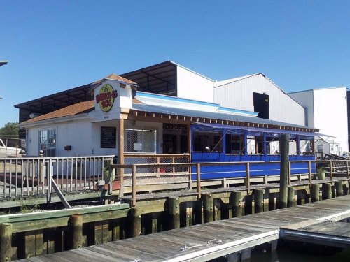 A waterfront restaurant with a blue exterior and outdoor seating, surrounded by docks and industrial buildings.